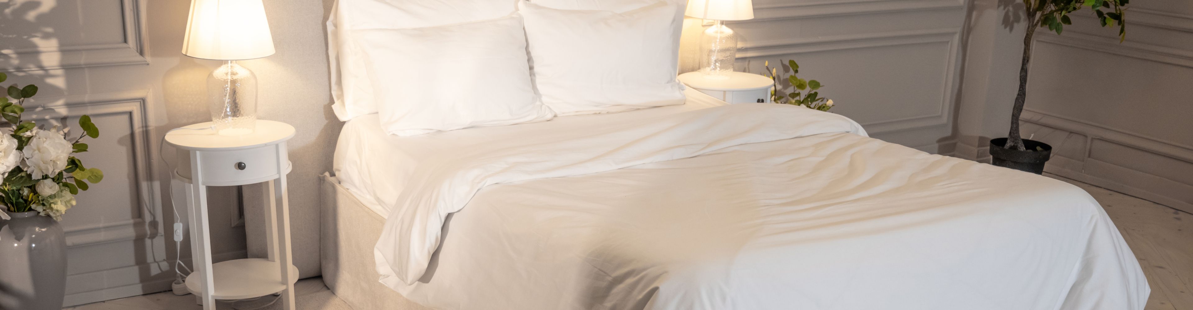 Hotel bed with white linens beside a bedside lamp